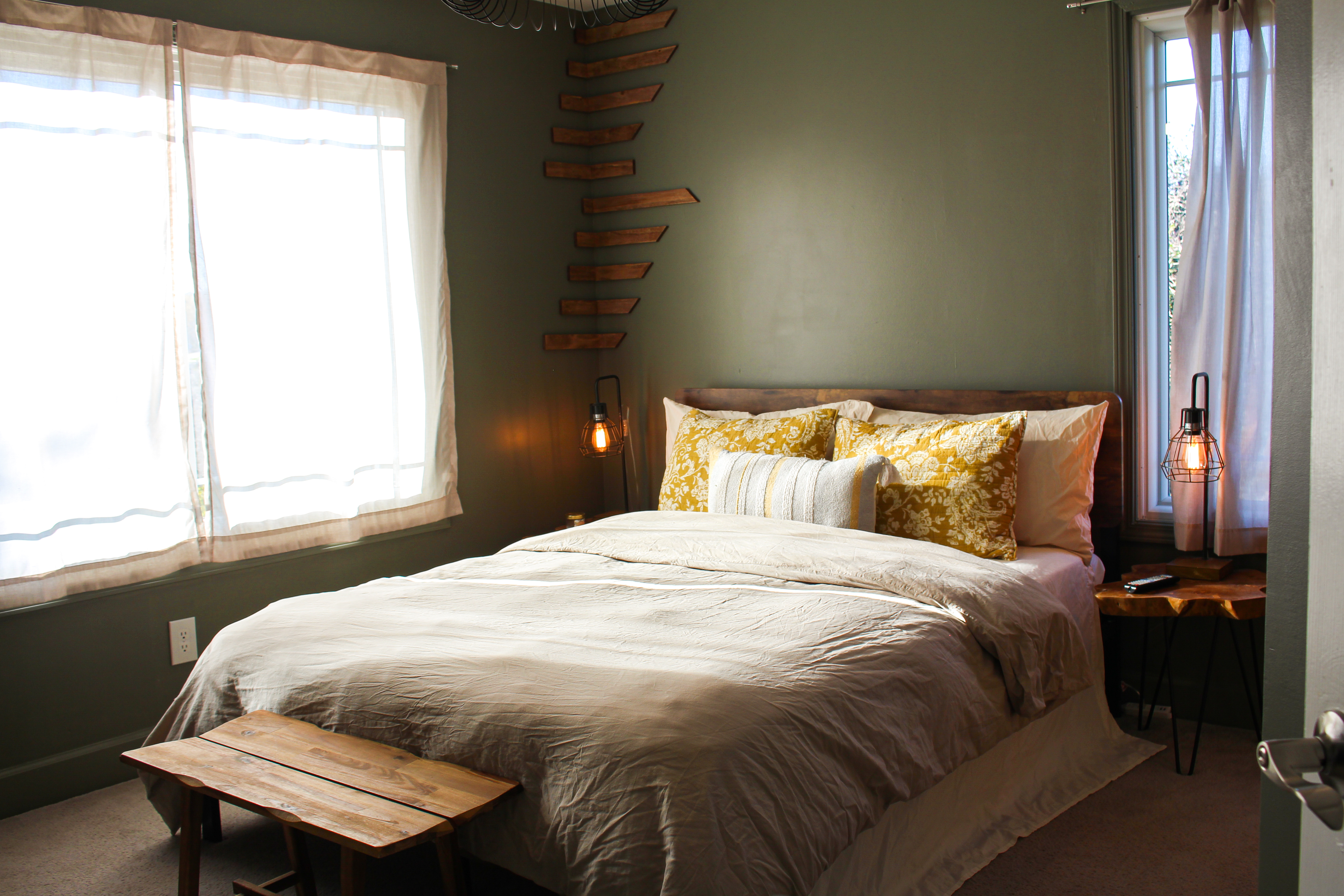 Bedroom with made bed, sage walls, and reclaimed-wood floating shelves